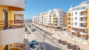 A coastal urban area with multi-story residential buildings, a wide road, and parked cars. - GuestReady - Sunshine at Costa da Caparica (Costa da Caparica)