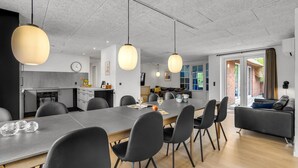 A modern kitchen with a dining area, featuring a large table, chairs, pendant lights, and a view of the outdoors. - Lovely home in Ulfborg with sauna (Ulfborg)