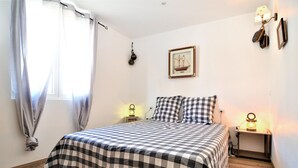 Een slaapkamer met een geruite sprei, een ingelijst kunstwerk aan de muur en twee bedlampen.