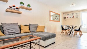 Een woonkamer met een bank, een glazen salontafel, een eethoek met een tafel en stoelen, en een spiegel aan de muur.
