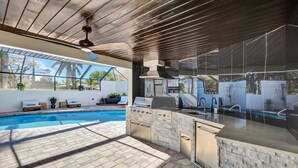Eine Außenküche mit Pool, integriertem Grill und Sitzbereich.