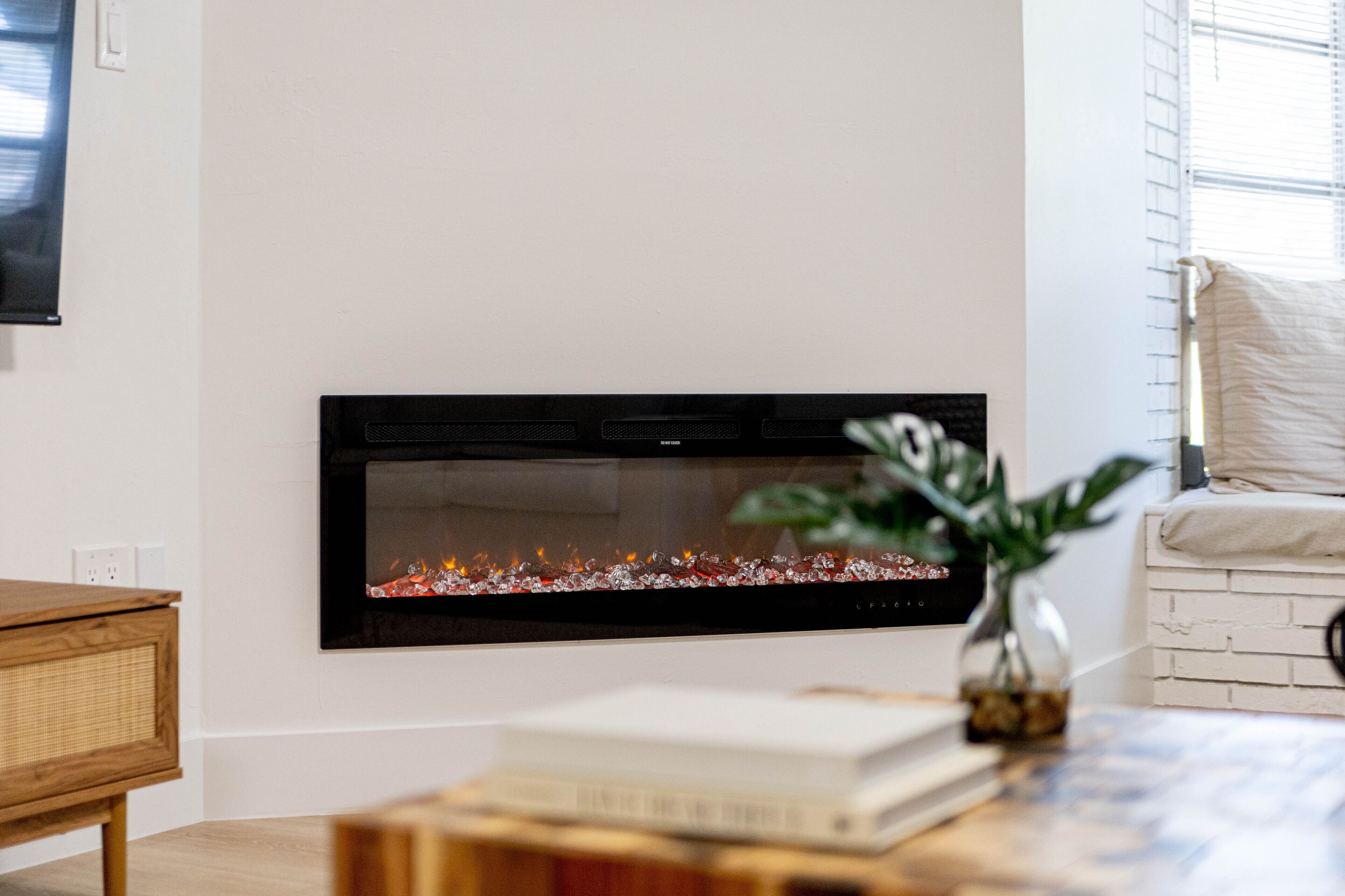 A modern living room with a fireplace, a wooden side table, a vase with a plant, and a bookshelf.