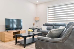 A modern living room with a flat-screen TV on a wooden stand, a black coffee table, a grey leather sofa, and a floor lamp.