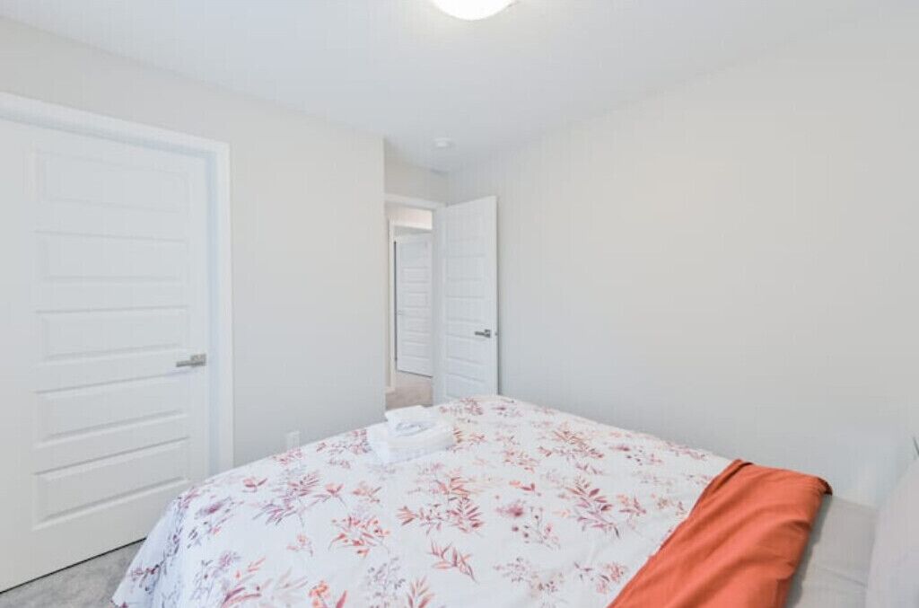 A bedroom with a bed, white walls, and a door leading to another room.