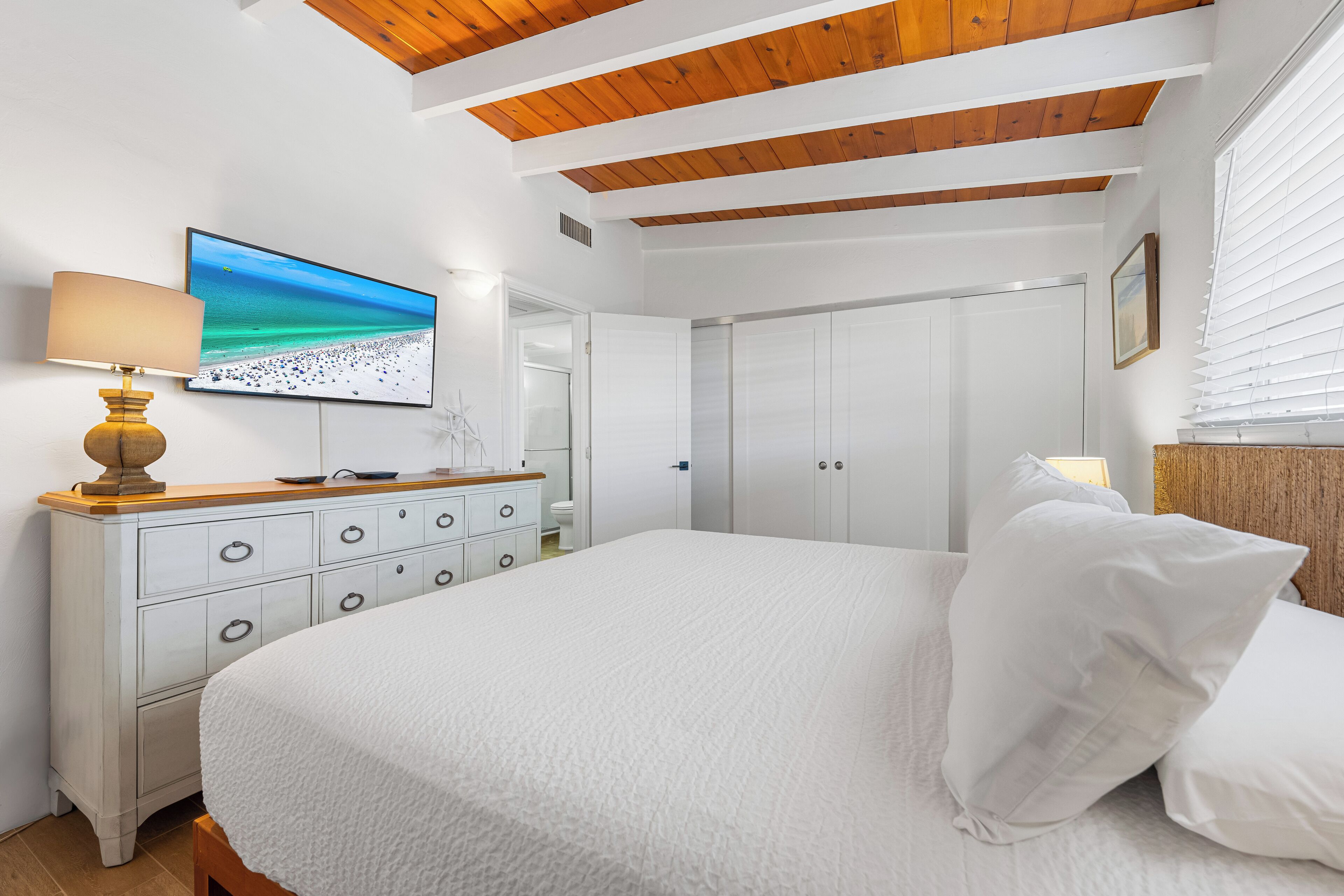Ein Schlafzimmer mit einem Bett, einem Schminktisch, einem an der Wand montierten Fernseher und einem Kleiderschrank.