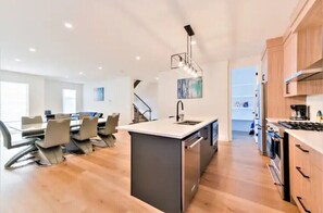 Enjoy cooking in the well-equipped kitchen with a central island, sink, and stove, adjacent to a dining area with a large table and chairs.