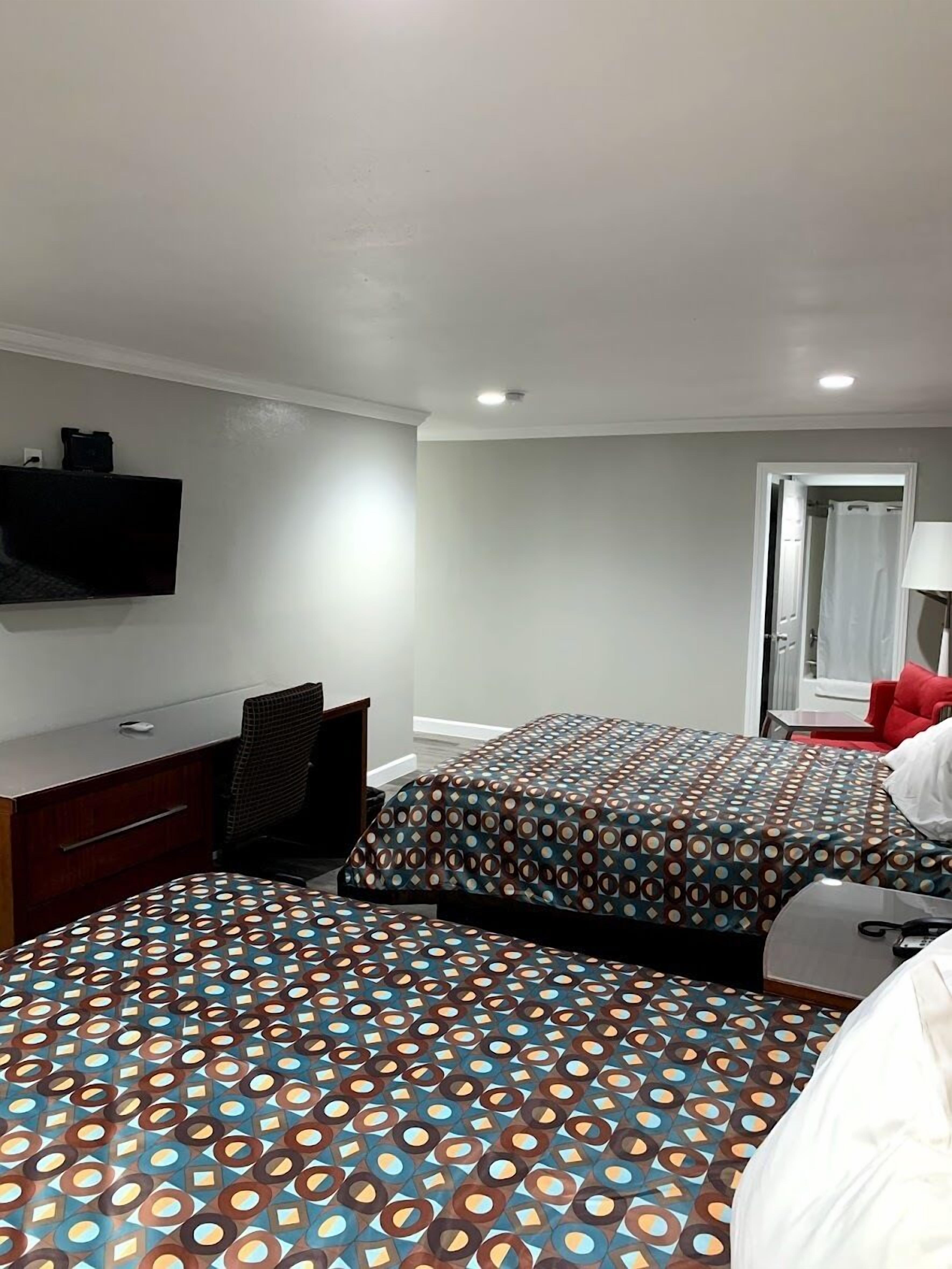 A hotel room with two beds, a desk, a chair, a TV mounted on the wall, and a bathroom visible through an open door.