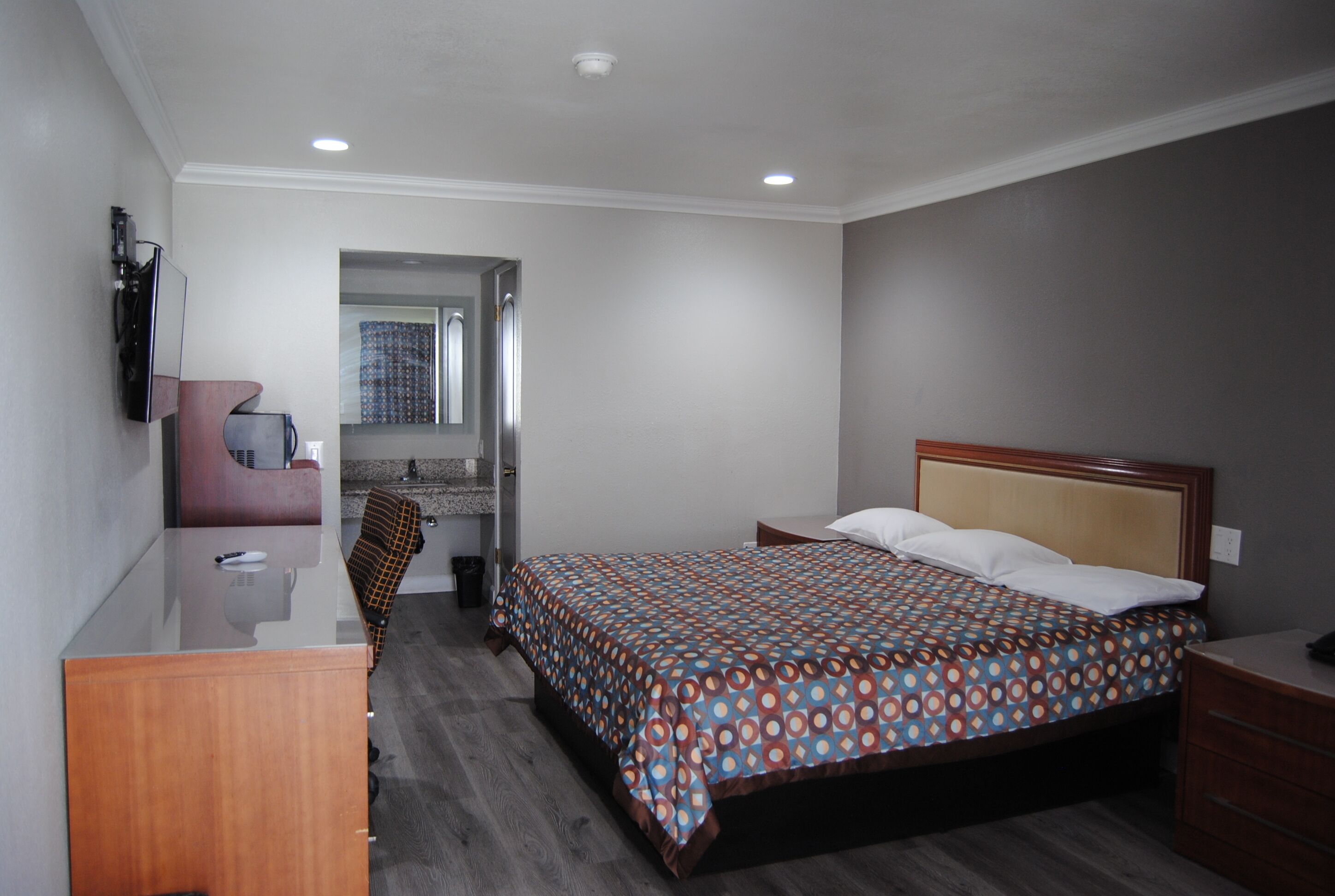 Habitación de hotel con cama, escritorio, silla, espejo y ventana con cortinas.