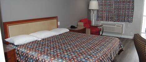 Habitación de hotel con una cama grande, un escritorio, una silla, una lámpara y una ventana con cortinas estampadas.