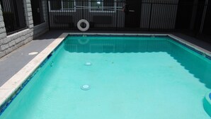 Ein rechteckiger Swimmingpool mit einer gefliesten Kante, einem schwarzen Metallzaun und einem Reifen an dem Zaun.