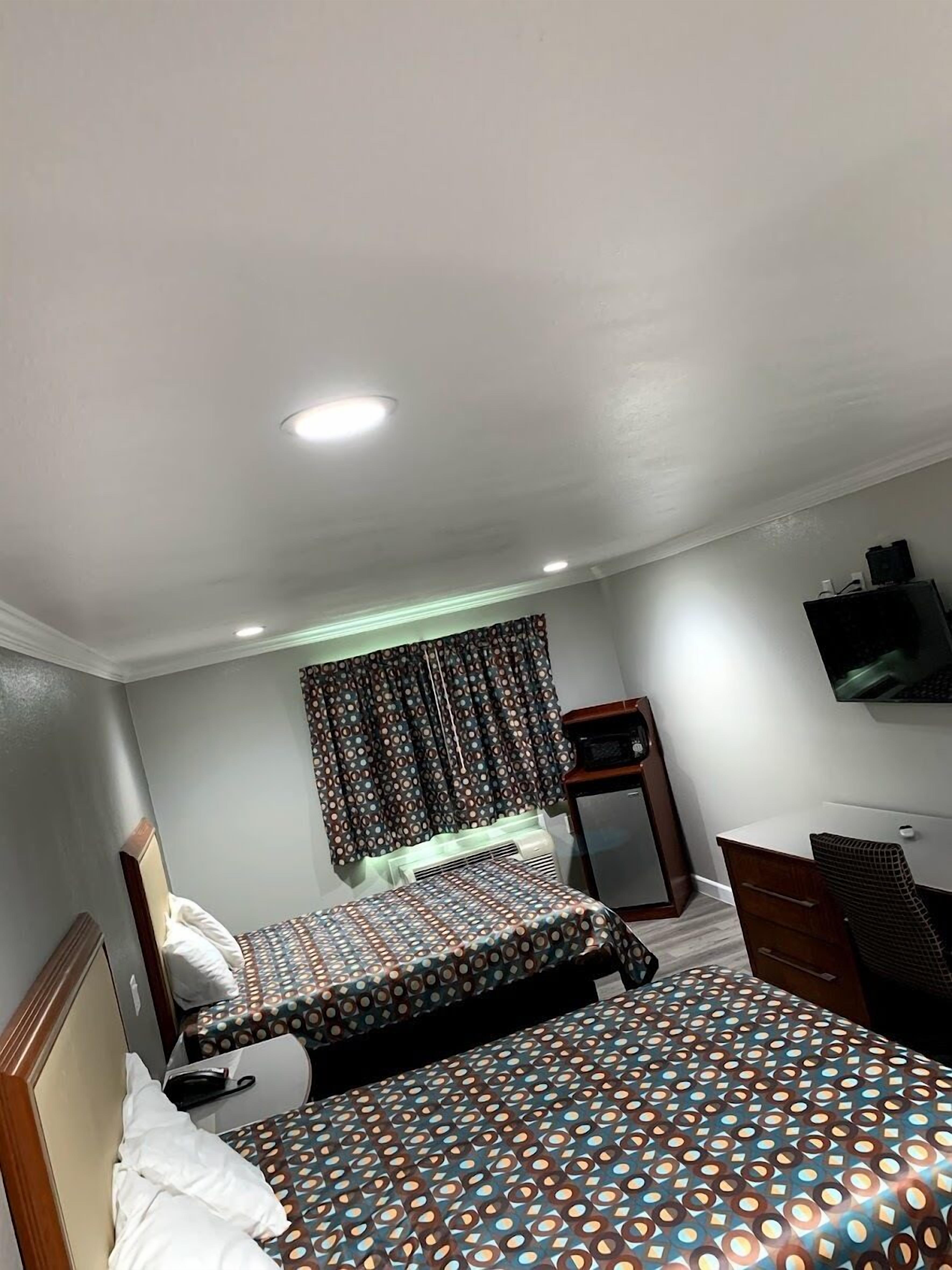 A hotel room with two beds, a desk, a television, and a window with patterned curtains.