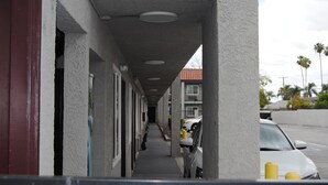 Ein Korridor mit einer Reihe von Fenstern und einer Tür links, einem überdachten Gang mit Geländer und geparkten Autos rechts.