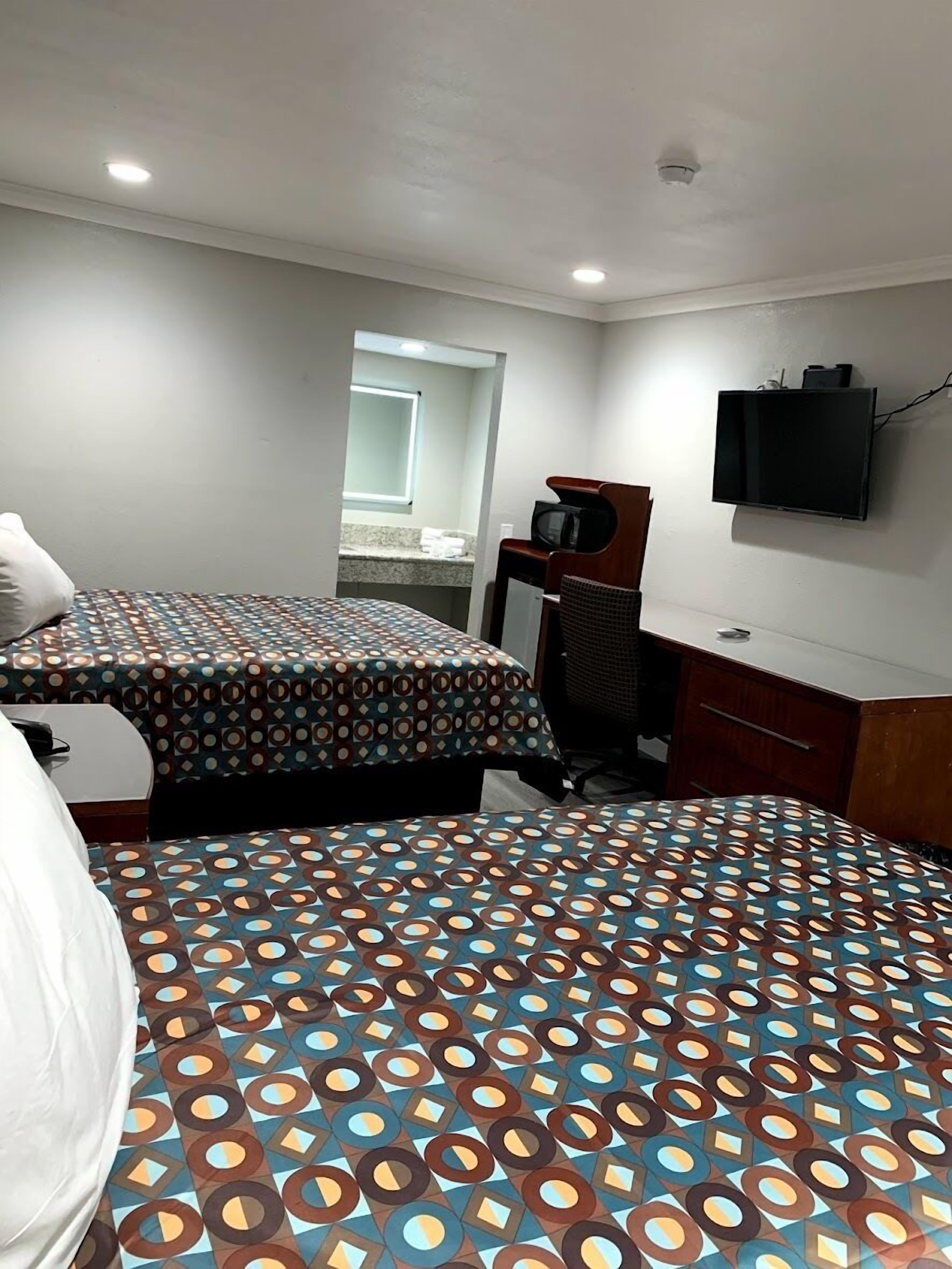 Ett hotellrum med två sängar, ett skrivbord, en tv och ett badrum som syns genom en öppen dörr.