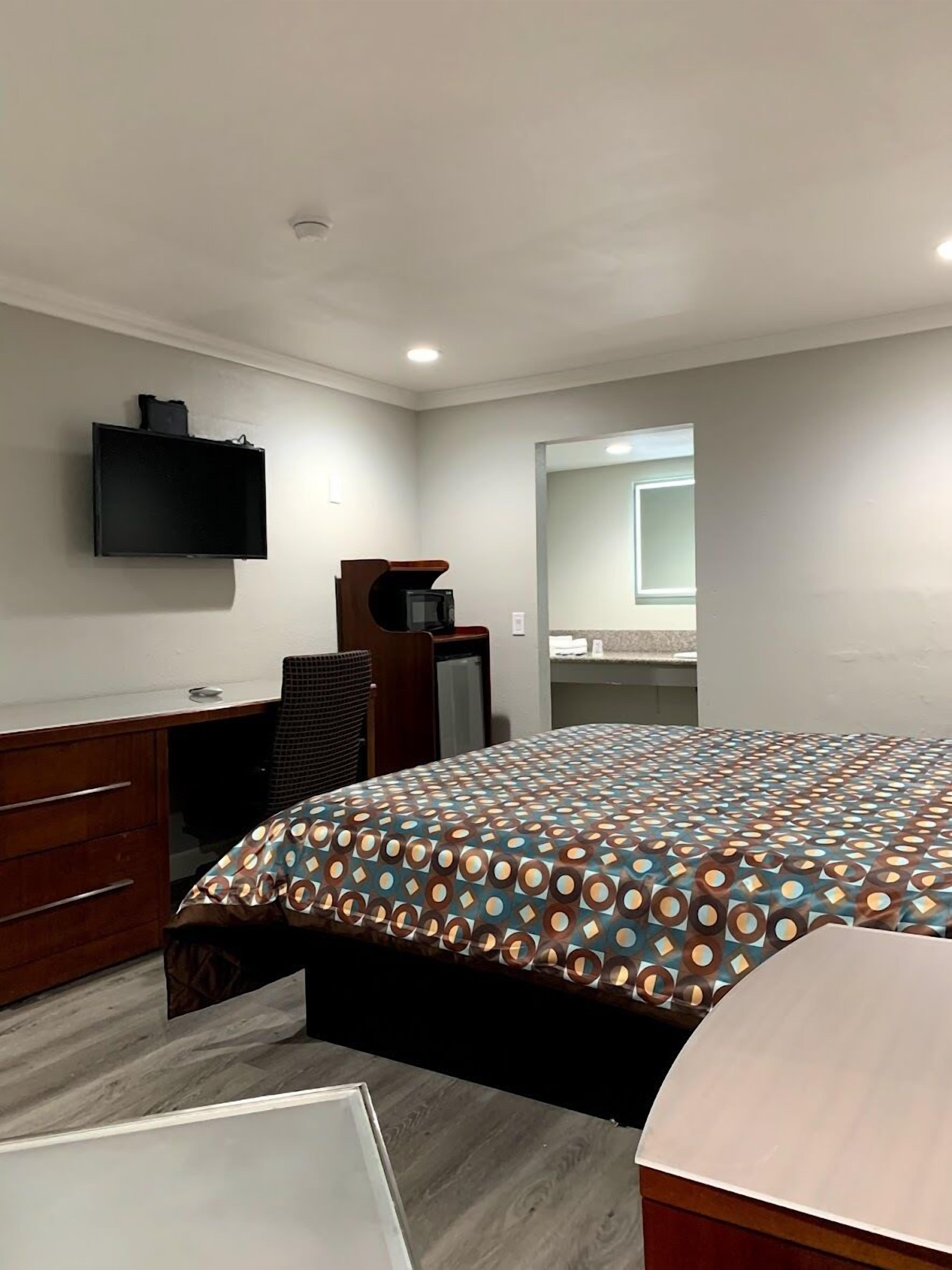 A bedroom with a bed, a desk, a chair, a TV, and a mirror.
