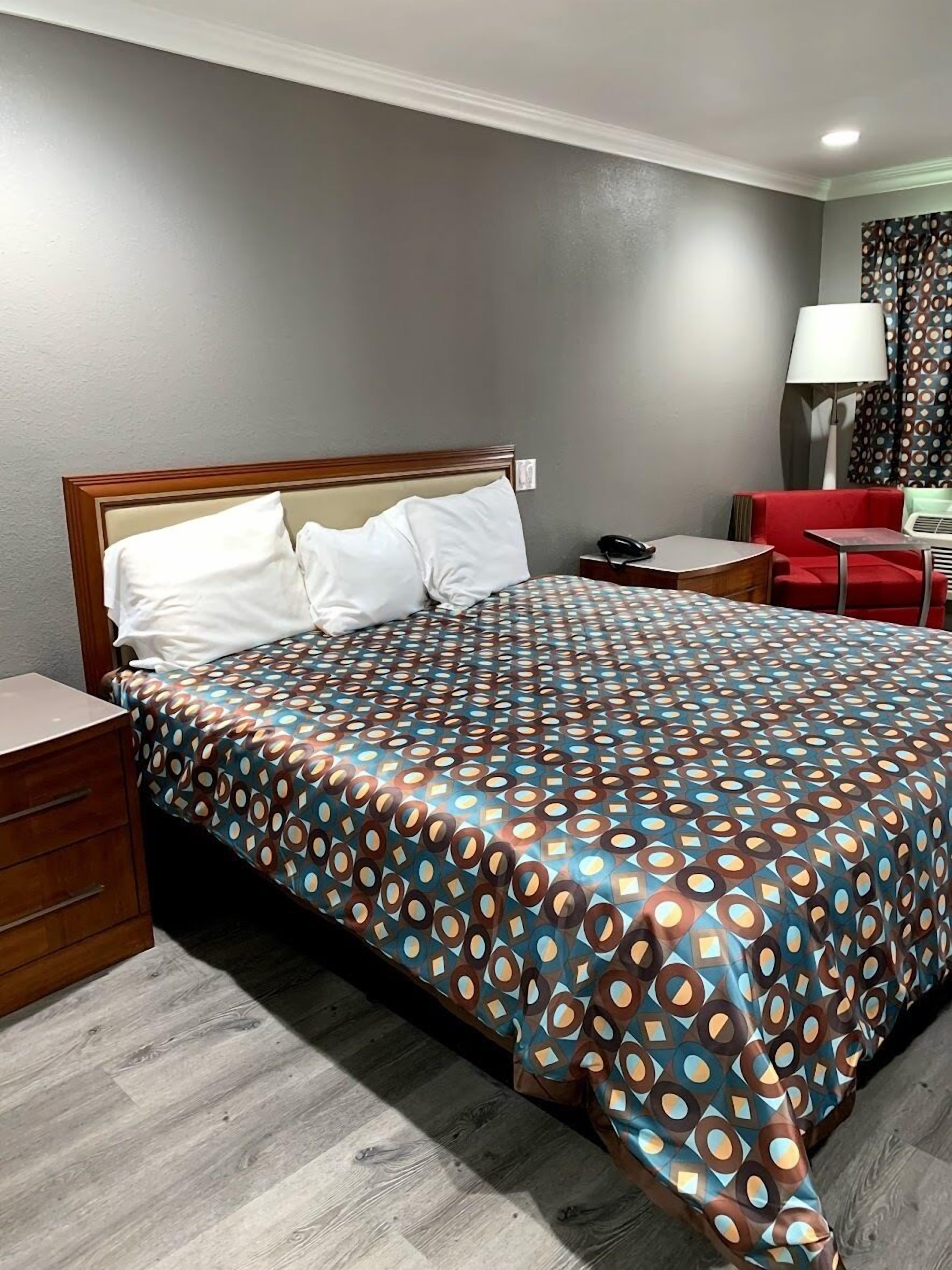 Une chambre d’hôtel avec un lit, une table de chevet, une chaise, une lampe et un canapé rouge.
