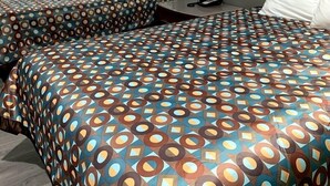 Ein Hotelzimmer mit zwei Betten, jeweils mit einem gemusterten Überwurf, einem roten Sessel, einer Lampe und einem Nachttisch.