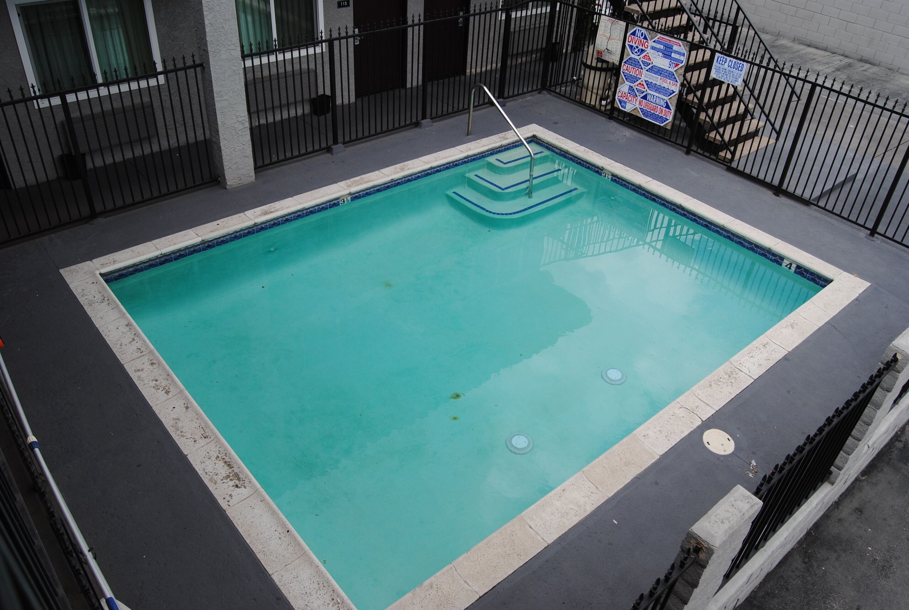A rectangular pool with a blue interior, surrounded by a black metal fence.
