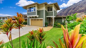 A two-story house with a garage, surrounded by well-maintained landscaping and a mountain in the background. - Ocean Views|Beach 6 Min|Private Hot Tub|Gated|BBQ (Waianae)