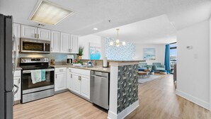 A modern kitchen with stainless steel appliances, white cabinetry, and a central island. - 3bedroom OceanView Condo - Sleeps 8 - Maximalist Beach Vacation Dream! (Myrtle Beach)