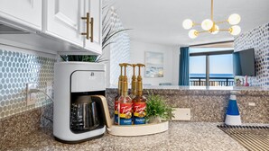 A modern kitchen with a coffee maker, Torani syrup bottles, and a potted plant. - 3bedroom OceanView Condo - Sleeps 8 - Maximalist Beach Vacation Dream! (Myrtle Beach)