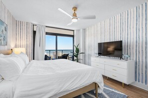 A modern hotel room with a large bed, a ceiling fan, a TV, and a balcony with a view. - 3bedroom OceanView Condo - Sleeps 8 - Maximalist Beach Vacation Dream! (Myrtle Beach)