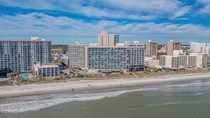 A beachfront hotel with multiple high-rise buildings, a swimming pool, and a beach in the foreground. - 3bedroom OceanView Condo - Sleeps 8 - Maximalist Beach Vacation Dream! (Myrtle Beach)