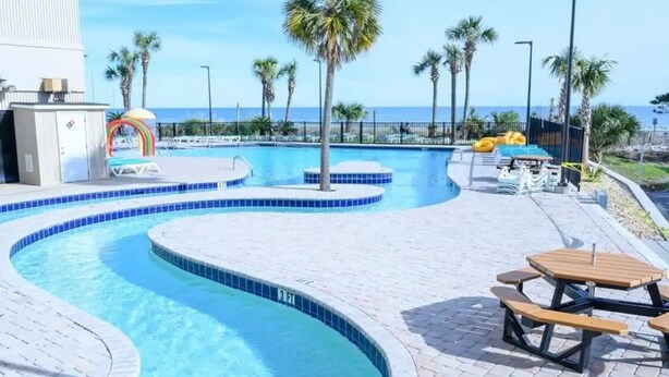 A swimming pool with a curved design, palm trees, and a beach view. - 3bedroom OceanView Condo - Sleeps 8 - Maximalist Beach Vacation Dream! (Myrtle Beach)