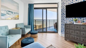 A modern living room with a sofa, ottoman, and a flat-screen TV mounted on the wall. - 3bedroom OceanView Condo - Sleeps 8 - Maximalist Beach Vacation Dream! (Myrtle Beach)