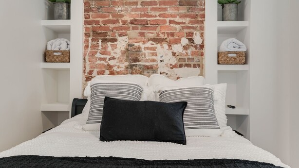 A bedroom with a brick wall, white shelving, and a bed with striped pillows. - Walk to the Naval Academy and Historic Annapolis.  Private parking at the home. (Annapolis)