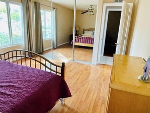 Ein Schlafzimmer mit einem Bett, einer Holzkommode und Blick durch eine Glastür in einen anderen Raum.
