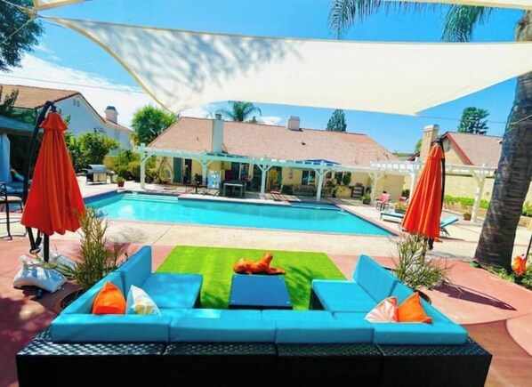 Ein Poolbereich mit einem blauen Außensofa, roten Sonnenschirmen und einer überdachten Terrasse.