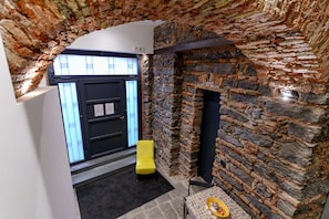 A stone-walled room with a black door, a yellow chair, and a small table with a plate.