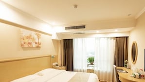 A hotel room with a large bed, a desk, a chair, a mirror, and a window with curtains.
