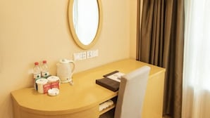 A hotel room with a wooden desk, a mirror, a kettle, and a chair.