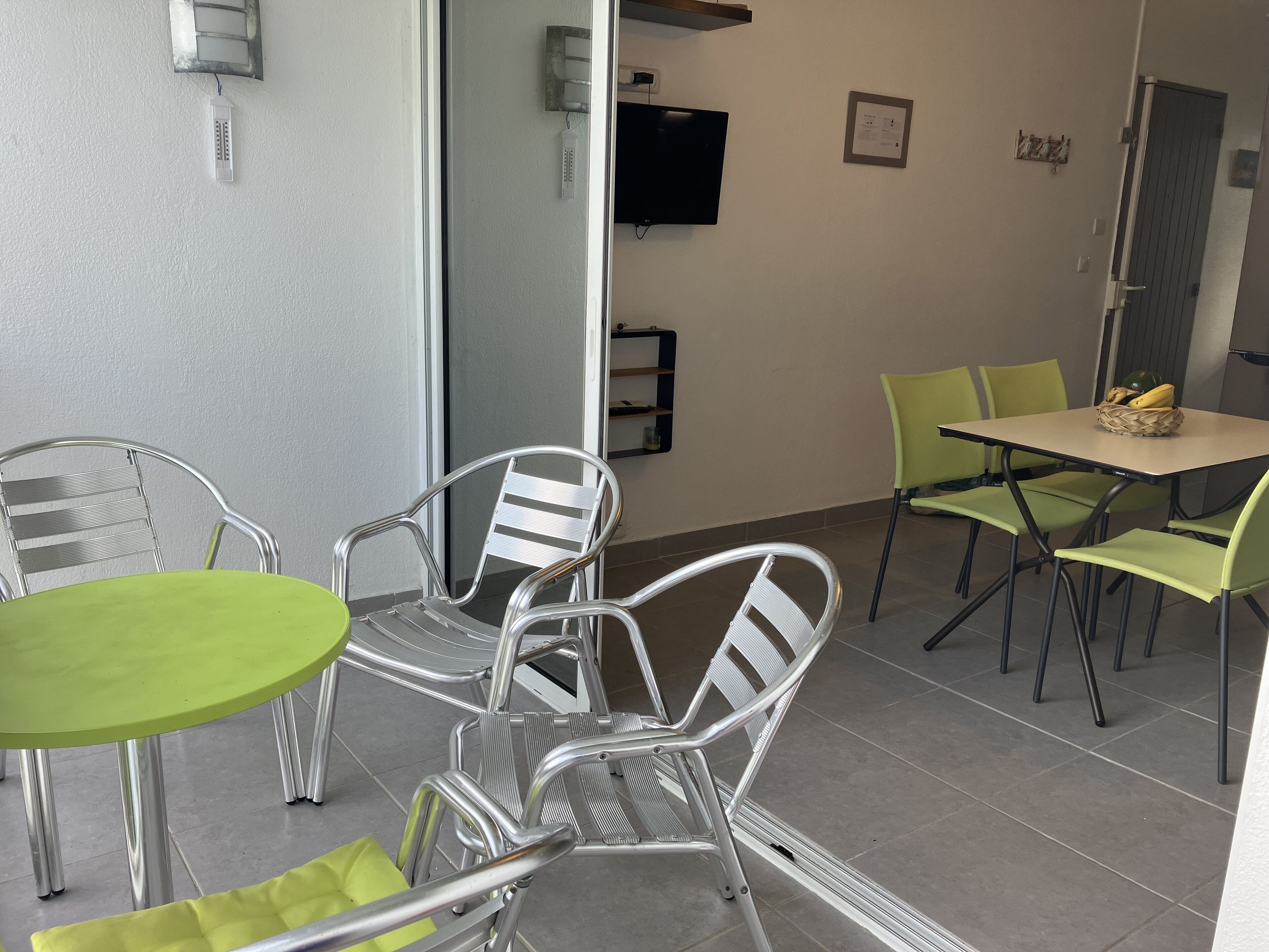 A dining area with metal chairs and a green table, a television mounted on the wall, and a door with a handle.