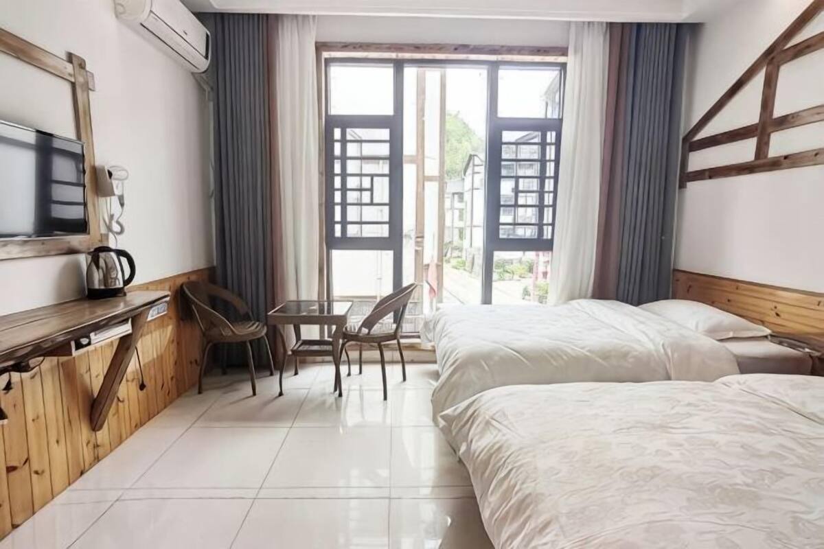 A hotel room with a bed, a desk with a chair, a television, and a window with curtains.