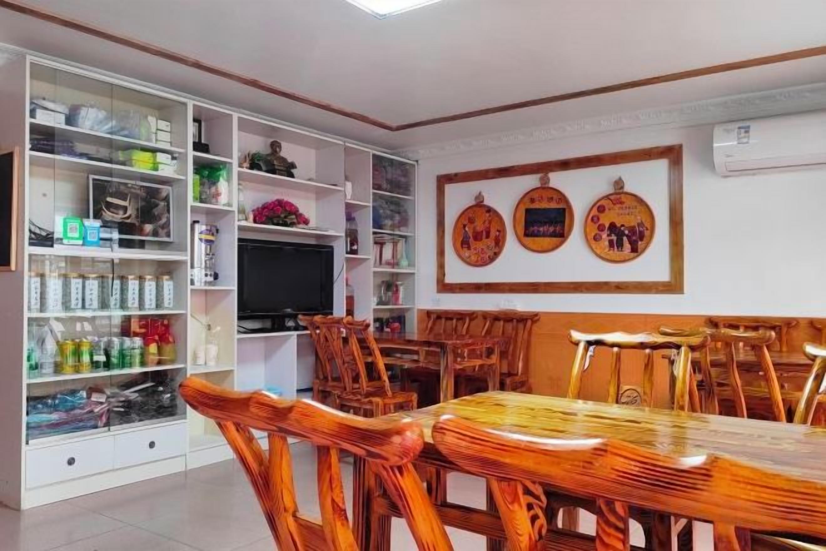 Un comedor con una mesa y sillas de madera, un televisor y un estante blanco con diversos objetos.