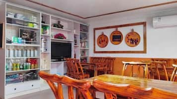 Un comedor con una mesa y sillas de madera, un televisor y un estante blanco con diversos objetos.