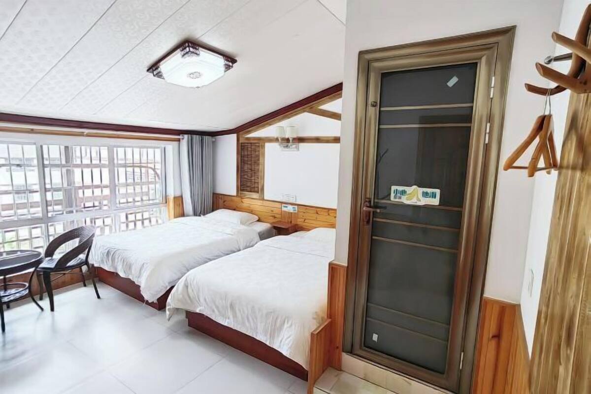 A hotel room with two beds, a small table, a chair, and a large window.