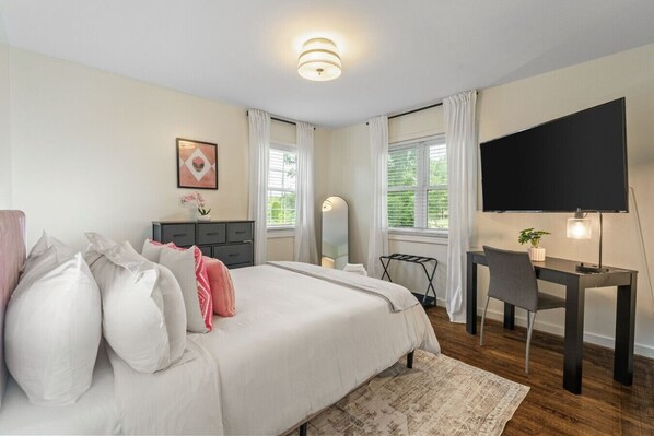Une chambre à coucher avec un lit, un bureau, une chaise, un téléviseur et une fenêtre avec des rideaux.