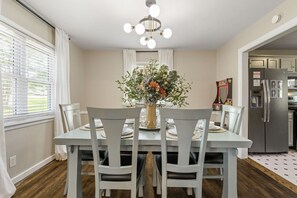 A dining area with a table set for four, surrounded by chairs, a vase with flowers, and a chandelier.