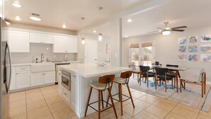 Een moderne keuken met witte kastjes, een groot eiland met barkrukken, en een eethoek met een tafel en stoelen.