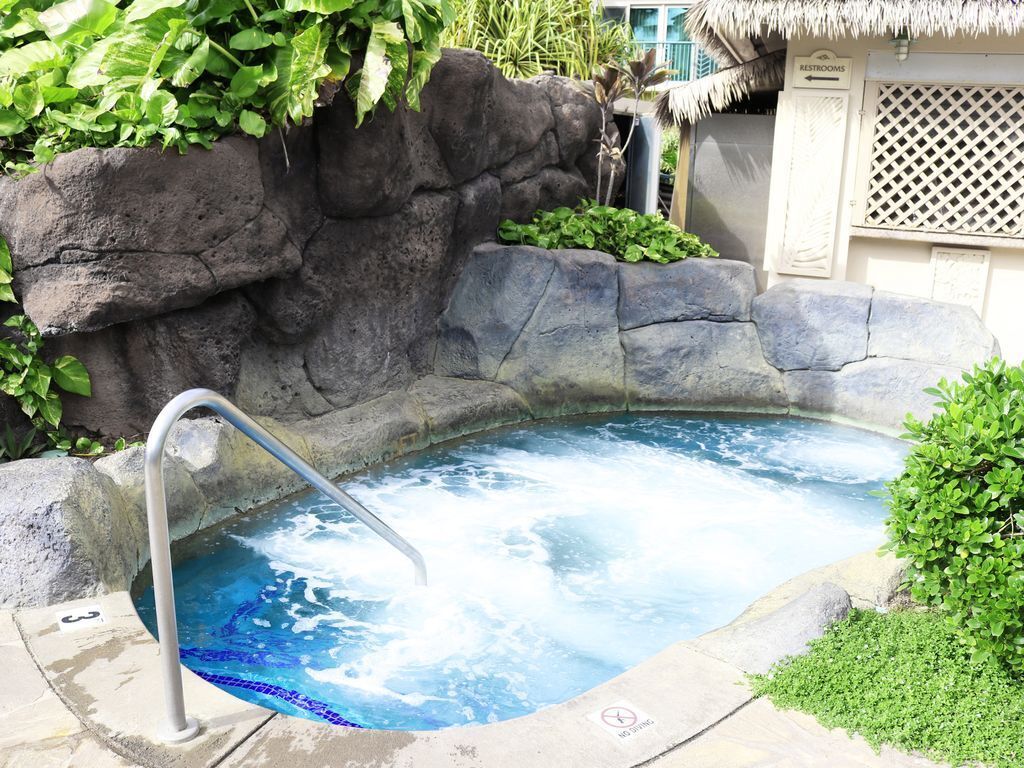 A hot tub with a metal ladder, surrounded by rocks and greenery.