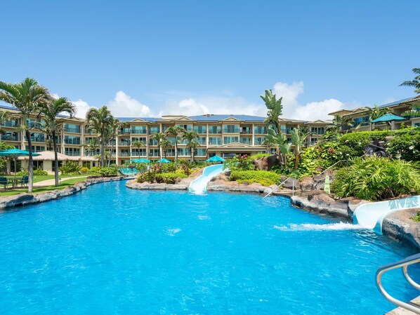A resort with a large pool, palm trees, and a waterfall.