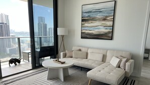 Un salon moderne avec un canapé d’angle, une table basse ronde et une grande fenêtre donnant sur la ville.