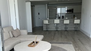 Un salon moderne avec une table basse ronde, un canapé et un coin cuisine équipé d’un four à micro-ondes et de tabourets de bar.