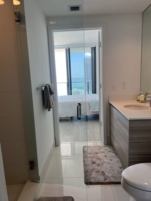 Ein modernes Badezimmer mit einer Glastür, die auf einen Balkon mit Bett und Blick auf die Stadt führt.