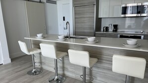 Une cuisine moderne dotée d’un îlot central, de tabourets de bar, d’appareils électroménagers en acier inoxydable et d’un design épuré et minimaliste.