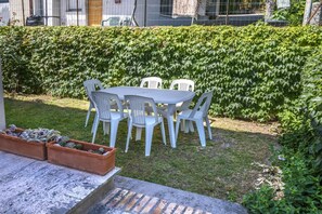 Une terrasse avec une table et des chaises, entourée d’une haie.
