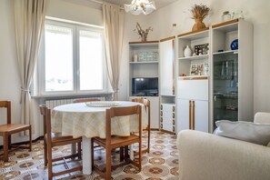 Un coin repas comprenant une table ronde et des chaises, un téléviseur et un meuble avec des étagères.